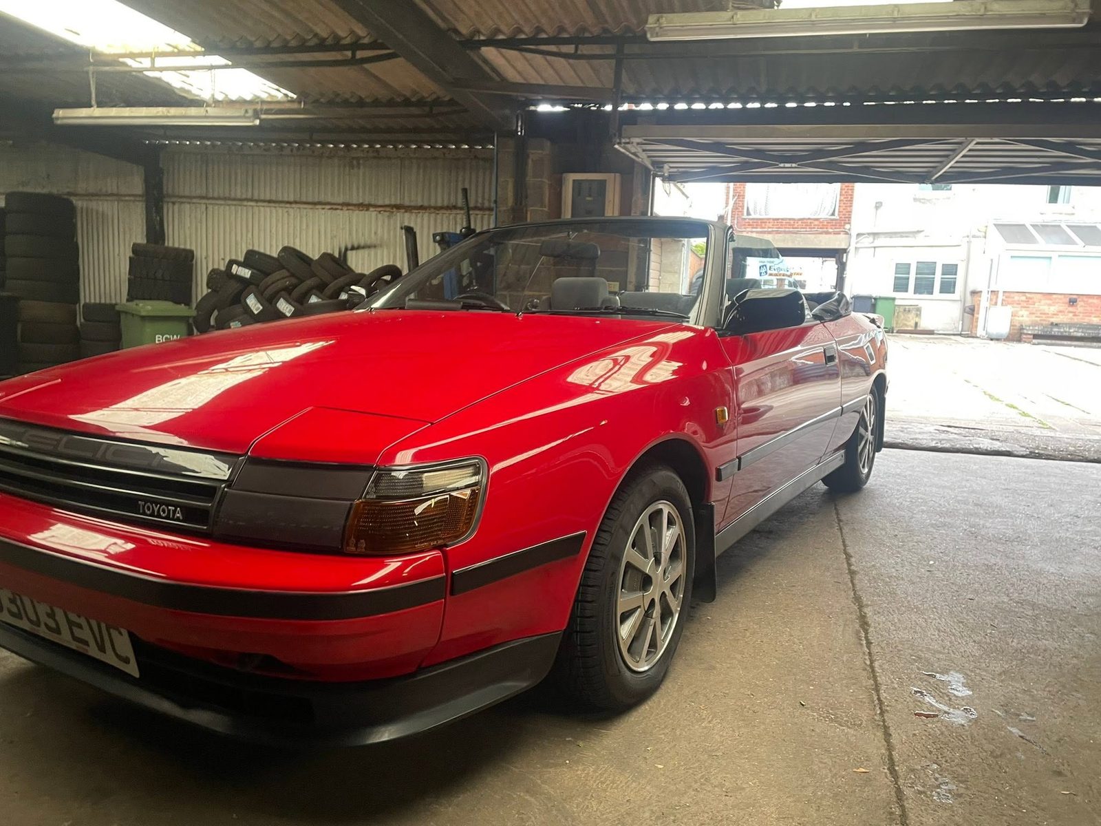 A red Toyota Celica convertible in the workshop with tyres stacked behind