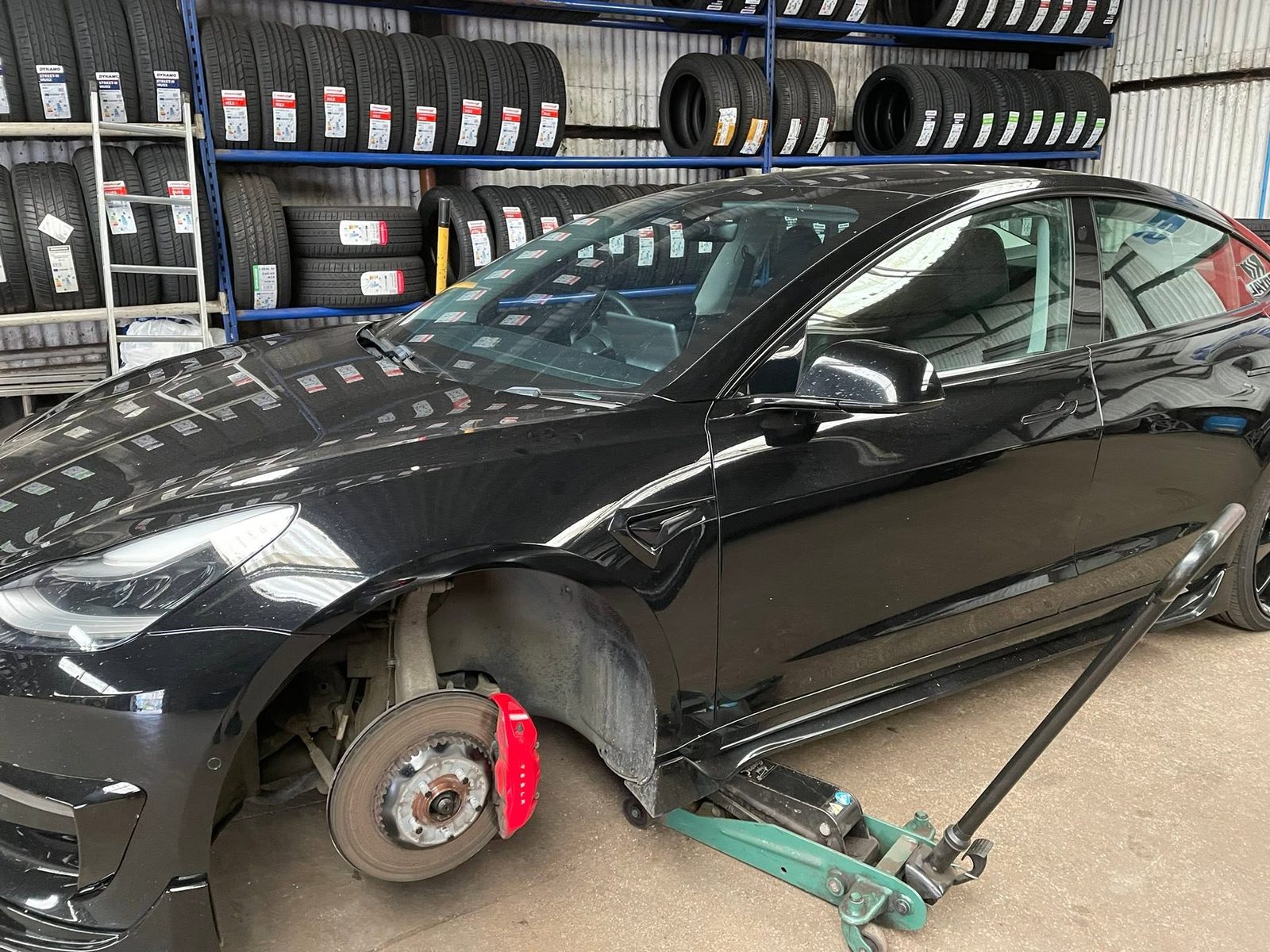 A black Tesla up on the trolley jack in front of a wall of racked tyres
